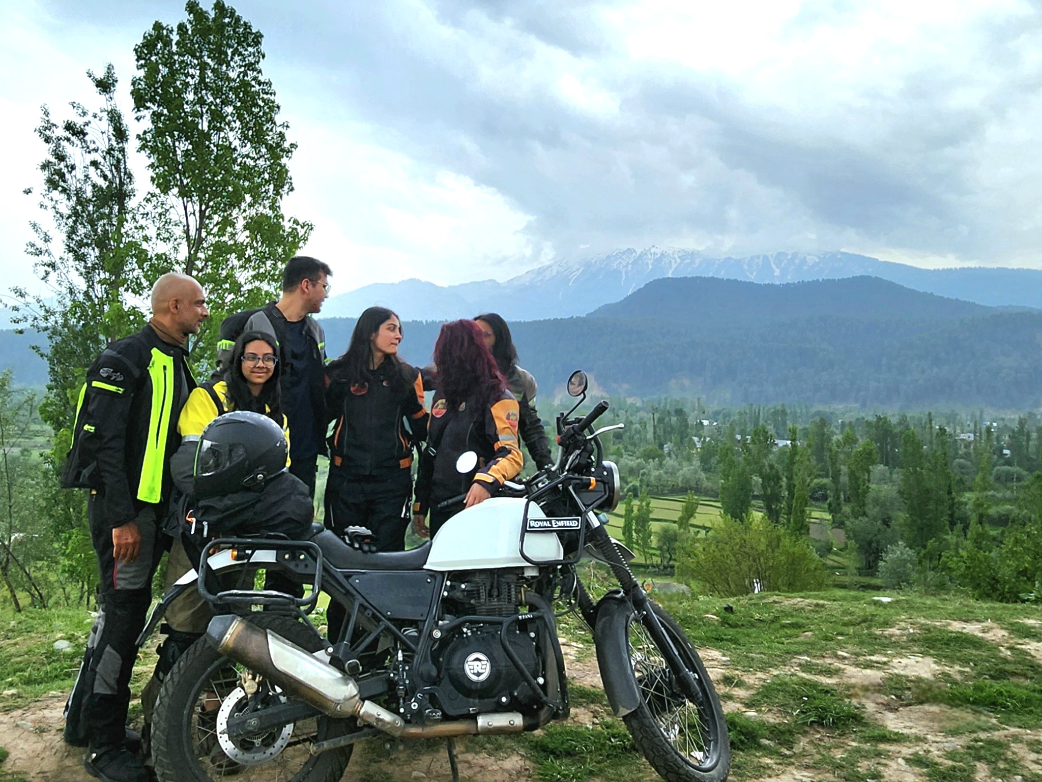 Small rider group beside a motorcycle in a valley.